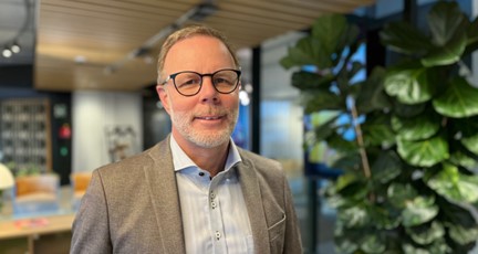 Man i grå kavaj, med glasögon ler mot kameran