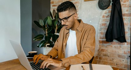 Man sitter vid bord och arbetar med laptop och anteckningsblock