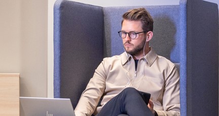 Man i galsögon, sitter i arbetsfåtölj och arbetar med laptop
