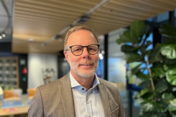 Man i grå kavaj, med glasögon ler mot kameran