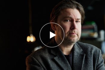 man tittar snett in i kameran, play-ikon i f&ouml;rgrund