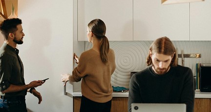 Man sitter framför laptop i köket på arbetsplatsen med två kollegor