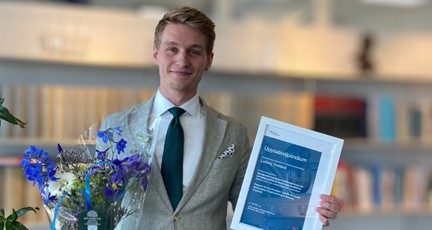 Vinnaren av Finansförbundets stipendium står med blombukett och diplom framför bokhylla